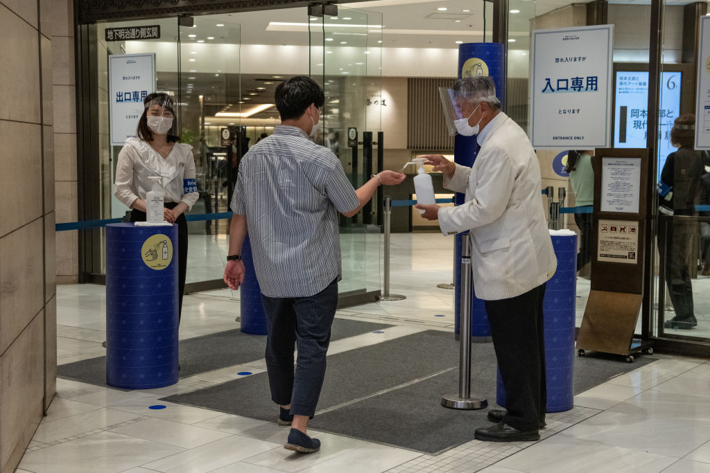 An employee sprays sanitizer onto the hand of an arriving customer
